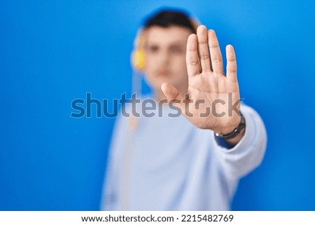 Non binary person listening to music using headphones doing stop sing with palm of the hand. warning expression with negative and serious gesture on the face. 