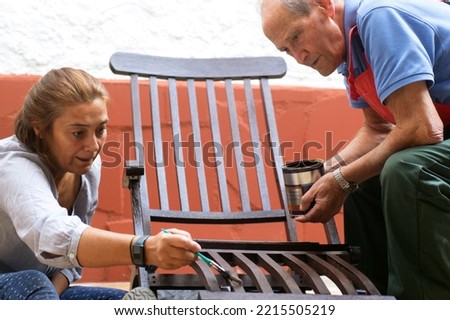 woman and senior man painting furniture to restore in old patio with flowerpots and whitewashed walls