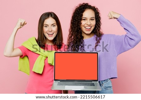 Young two friends happy IT women wear green purple shirts together hold use work on laptop pc computer with blank screen workspace area do winner gesture isolated on pastel plain light pink background