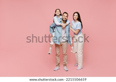Full body young parents mom dad with child kid daughter teen girl in blue clothes giving piggyback ride to kid, sit on back isolated on plain pastel light pink background Family day childhood concept Royalty-Free Stock Photo #2215506659