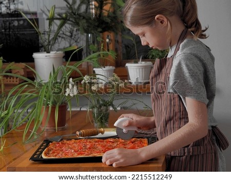 A young boy in an apron demonstrates a pizza prepared at home against the background of a kitchen cabinet. Healthy home cooking.