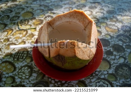 peeled coconut with a straw inside on a patterned table ready to drink
