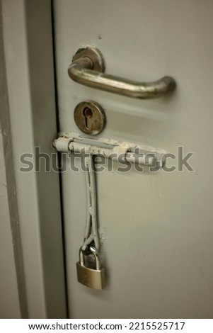 close up view of metal emergency door with door handle, key hole, and padlock