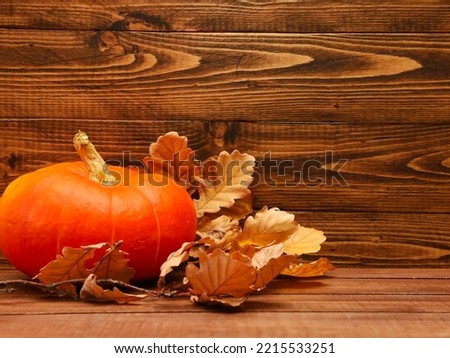 Orange pumpkin, dry yellow oak leaves on wooden table at brown rustic wood barn wall background. Autumn, fall menu, holiday, thanksgiving, harvest season