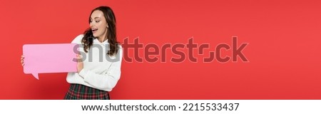 Pretty young woman in sweater holding speech bubble isolated on red, banner