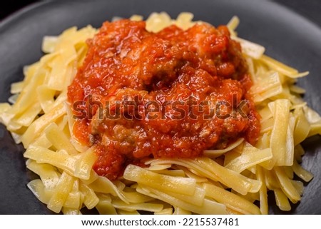 Spaghetti with meat balls in tomato sauce in a black bowl on a dark concrete background