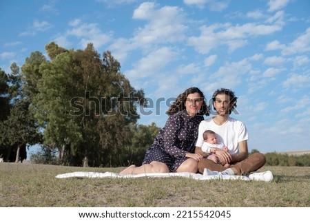 Smiling multiracial couple and their daughter on vacation in nature resting relaxed with family during the picnic. Happy portrait of a family in nature with their baby.