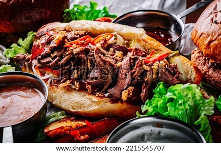 Philly cheese steak sandwich with meat, vegetables, cheese and sause on wooden table. street food Royalty-Free Stock Photo #2215545707