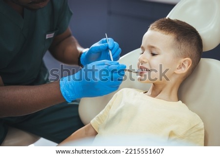 Dentist doing regular dental check-up to little boy. Close up of boy having his teeth examined by a dentist. Cute boy smiling while teeth exam . Happy boy sitting in dentists chair 