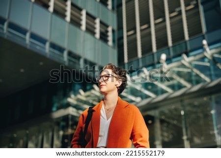 Low angle view of a mature businesswoman listening to music on earphones while commuting to work in the city. Thoughtful businesswoman walking to her office in the morning. Royalty-Free Stock Photo #2215552179