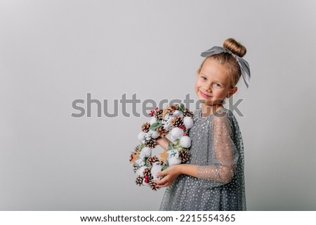 a 7-year-old girl in a festive silver dress with a New Year's wreath in her hands on a gray background