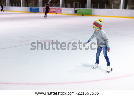 Adorable little girl wearing jeans, warm sweater and colorful hat skating on ice rink