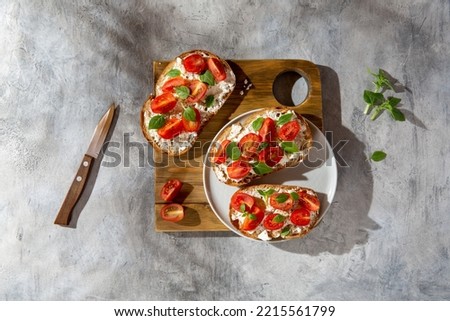 Sandwich with cottage cheese, tomatoes and basil on concrete background. Traditional Italian bruschetta. Healthy savory feta and tomato toast. Top view. Royalty-Free Stock Photo #2215561799