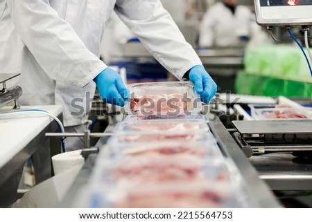 Close up of a meat industry worker gathering packed meat on a conveyor belt. Royalty-Free Stock Photo #2215564753