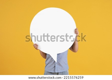 Kids opinion matters. Studio portrait of unrecognizable little boy hiding behind speech bubble with empty space, orange background Royalty-Free Stock Photo #2215576259