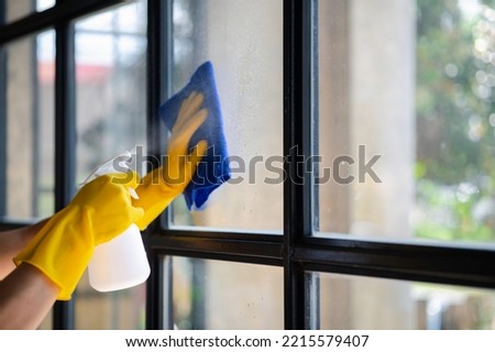 Person cleaning the room, cleaning staff is using cloth and spraying disinfectant to wipe the glass in the company office room. Cleaning staff. Maintaining cleanliness in the organization. Royalty-Free Stock Photo #2215579407