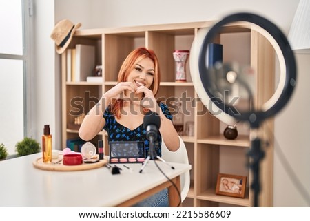 Young caucasian woman applying make up doing tutorial smiling in love showing heart symbol and shape with hands. romantic concept. 