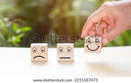 Hand picks up a wood block with a smiling emblem with his hand. A survey, poll, or questionnaire designed to gather information about user experience or customer satisfaction.