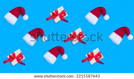 Red Christmas Santa hat and gift box with tied red bow on the blue background. Pattern. Flat lay.
