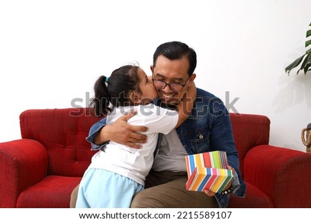 Asian little girl kissing her father while giving fathers day gift