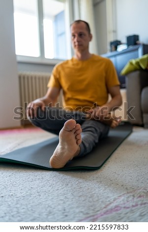 Focus on bare foot. A Man on a mat doing some exercise at home. Bright Apartment with Minimalistic Interior. Handsome man doing stretching exercise at home. Concept of healthy life.