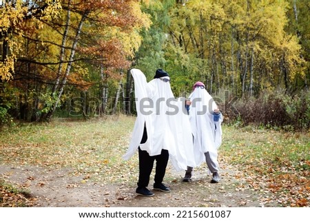 Happy two people in a ghost costume on the background of the forest. Halloween Autumn. The concept of a scary and merry holiday.