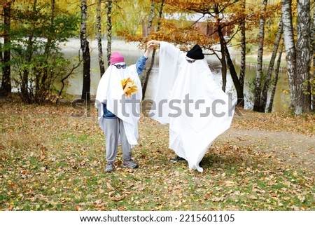 Happy two people in a ghost costume on the background of the forest. Halloween Autumn. The concept of a scary and merry holiday.