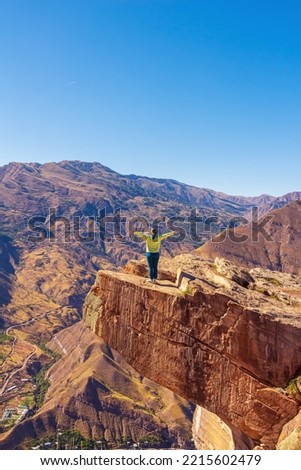 Girl tourist on an extreme ledge in the rock Troll tongue. View of the Caucasus Range, Dagestan. Royalty-Free Stock Photo #2215602479