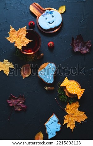 Autumn tea. Cup of tea, painted gingerbread, acorns and leaves on a black background.
