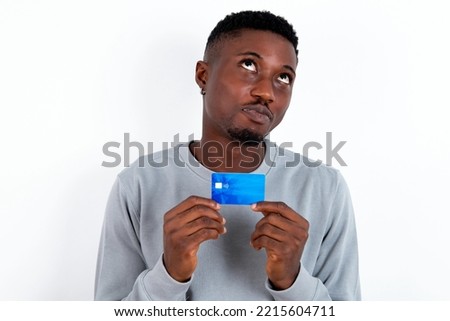 Photo of cheerful young handsome man wearing grey sweater over white background hold debit card look empty space