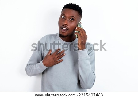Smiling young handsome man wearing grey sweater over white background   talks via cellphone, enjoys pleasant great conversation. People, technology, communication concept