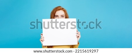 Close up Portrait young beautiful attractive redhair girl smiling showing blank sign. Blue Pastel Background. Copy space