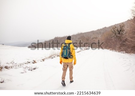 Maxk view of the man dresssed yellow warm jacket and trousers, bagpack traveling in the snow landscape