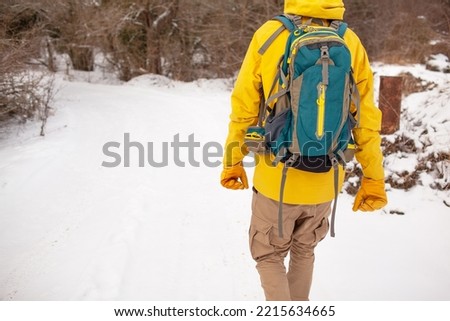 Maxk view of the man dresssed yellow warm jacket and trousers, bagpack traveling in the snow landscape