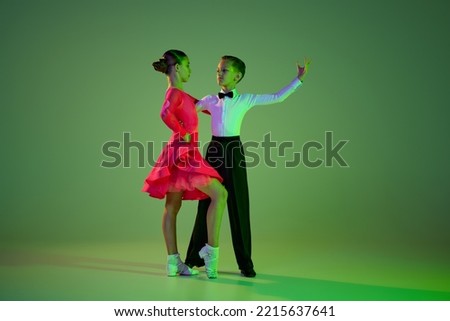 Cha cha cha, rumba, tango. Full-length portrait of beautiful little boy and girl dancing ballroom dance isolated over background in neon light. Concept of art, beauty, grace, action, emotions. Royalty-Free Stock Photo #2215637641