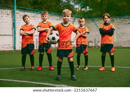 Teammates. Athletic boys in junior soccer team standing together at grass sport field. Football players in orange-black kits and boots. Concept of sport, studying, achievements, success and skills