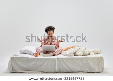 News, wow. Surprised young charming girl in home wear sitting on bed at home isolated on gray background. Ideas, inspiration, imagination. Art, beauty, youth and emotions.