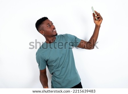 Portrait of a young handsome man wearing green T-shirt over white background taking a selfie to send it to friends and followers or post it on his social media.
