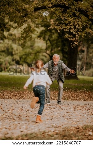 Handsome grandfather spending time with his granddaughter in park on autumn day Royalty-Free Stock Photo #2215640707