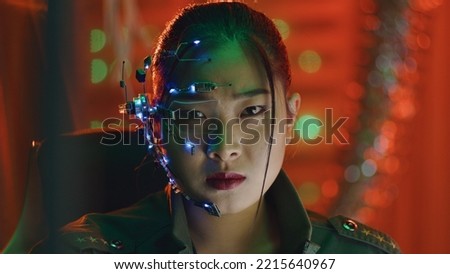 A Cyberpunk girl looks at the computer screen. Wearing futuristic one-eyed glasses with microphone. Stops looking at the computer to face the camera. Cyber and sci-fi backgrounds.