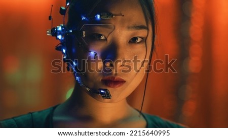 Asian girl in Cyberpunk style with a head set and microphone with small white LED lights looks at the camera. Intense facial expressions. Sci-fi background with Neon lights.