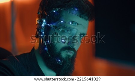 Brunette guy works on the computer with neon lights in background. Cyberpunk. Wearing a futuristic one-eyed glasses and microphone. Cyber and sci-fi backgrounds.