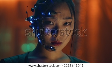 Asian girl in Cyberpunk style with a head set and microphone with small white LED lights looks at the camera. Intense facial expressions. Sci-fi background with Neon lights.