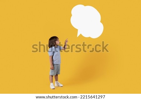 Interesting news. Cute little boy looking at blank speech bubble, pointing with finger, standing over orange studio background, empty space Royalty-Free Stock Photo #2215641297