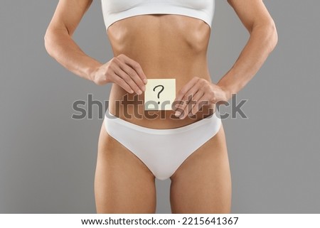 Women's Health. Young Female In White Underwear Holding Card With Question Mark Near Her Belly, Closeup Shot Of Unrecognizable Slim Lady In Panties Posing Over Grey Studio Background, Copy Space