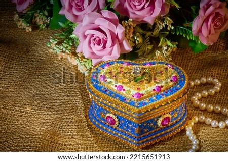 the beautiful box is shot on a brown cloth background with a necklace of pearls and pink flowers , can be used as a greeting card