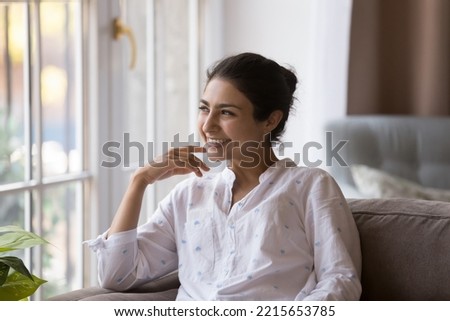 Young millennial dreamy Indian woman smile staring into distance while relaxing on cozy couch at modern home, enjoy daydreams and carefree weekend leisure feels happy, spend free time alone indoors Royalty-Free Stock Photo #2215653785