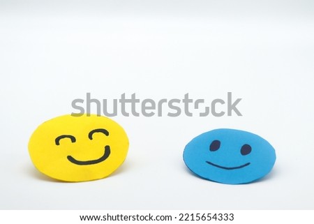 two happy smiling faces, made of blue and yellow paper cut out on a white background. Concept of well-being, happiness, companionship, kindness