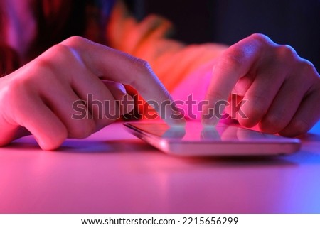 Use of mobile phone in trendy neon lights. Creative vivid color of ultraviolet red and blue. Hands of Teen Girl scrolling up photos Close-up at dark neon room. App for sale in shop. Social media.