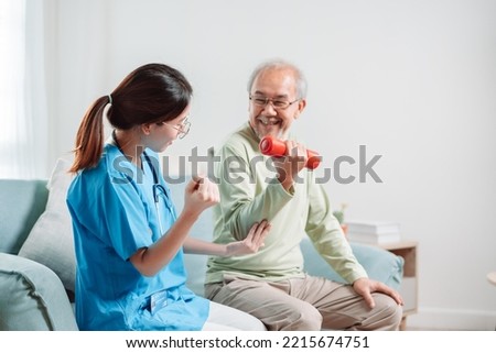 Asian Senior old man doing physiotherapist with support from caregiver. Mature male sitting on sofa in living room using dumbbell workout exercise. Healthcare medical concept. Royalty-Free Stock Photo #2215674751